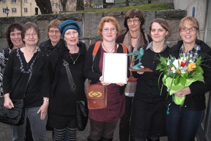 Personalen från Korallen och Lagunen står utanför Landstingshuset. Blommor, en tavla med prismotivering och en statyett med en fågel finns också med på bilden.