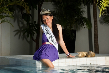 Foto: Gorm K Gaare. Miss Landmine Cambodia 2009. Fotot är på Song Kosal som kom tvåa i tävlingen. Hon sitter med det ena benet i vattnet vid en pool. I det mörka långa håret har hon en tiara. Det andra benet slutar i jämnhöjd med knäet som man skönjer under den lila klänningen. Över Song Kosals axeln hänger miss-banderollen.