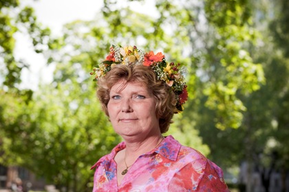 Annika Östberg har ljust lockigt hår, blomsterkrans i håret och färgglad klänning