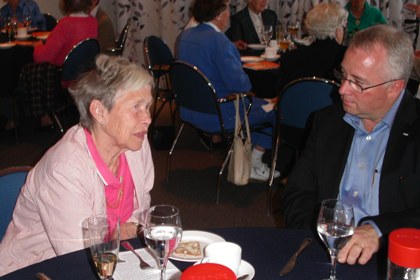 På foto från Synskadades Riksförbund Lidingös 50-årsjubileum 2009 sitter medlemmen Helena Lovén och kommunalrådet i Lidingö stad  Paul Lindquist och samtalar vid ett matbord.