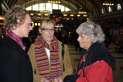 Monica Fallenius har kort ljust hår, mörk kappa och rosa scarf, Anne-Helene Järverup har ljust uppsatt hår, ljus jacka långsmala glasögon och randig halsduk i flera färger. De samtalar med Anna Sonmark i röd jacka och grått hår.