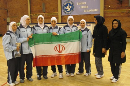 Det iranska damlaget i goalball efter segern i Stockholm. De har blåa träningsoveraller, vit huvudduk som täcker hår och hals och de håller en pokal och en stor iransk flagga