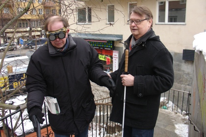 Gatukontorets kommunikatör Mats Freij prövar att ta sig upp för trappan mellan Gotlandsgatan och Götgatan. Han bär fingerad optik. Han har stöd av Guy Perdhe ombudsman på SRF Stockholms Gotlands lan.