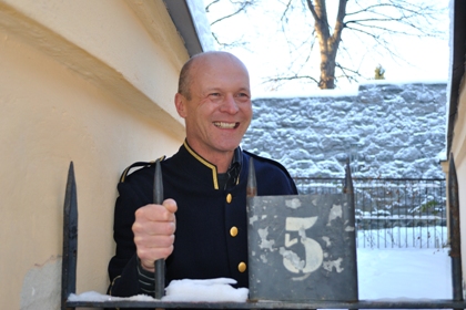 Ola Nyman har långsmalt ansikte, kort hår och en gammal fångvaktarjacka i mörkblått med mässingsknappar.