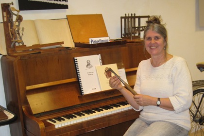 Gilda Stiby sitter framför ett piano och håller ett långsmalt instrument i handen.