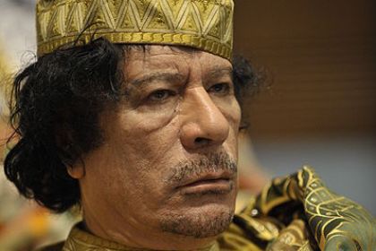 Libyens ledare Muammar al-Gaddafi. Han har mörkt lockligt hår, han bär hätta och skjorta i guldfärgat tyg