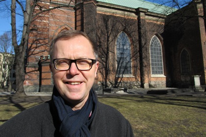 Hans Öjmyr är utställningschef på Stadsmuseet bär glasögon med mörka bågar. Har kort cendrèfärgat hår, svart halsduk och en mörk rock.