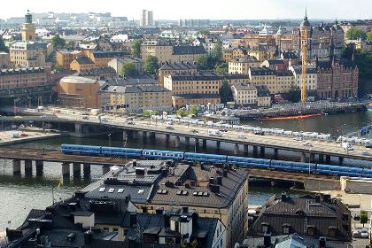 Vy över stockholm tagen från gamla stan mot södermalm. I förgrunden hustaken i Gamla Stan. En tunnelbana syns på avstånd på väg mot Slussen, och även bilar på centralbron.