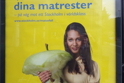 Annonstavla med bild på ung kvinna som håller i ett väldigt stort äpple.