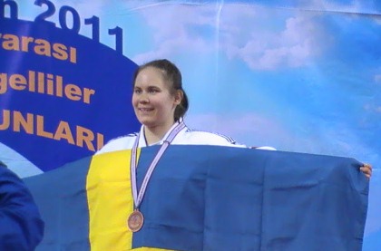 Nicolina Pernheim med vit judodräkt och  en guldmedalj runt halsen vid EM i London i november. Nicolina håller upp en svensk flagga framför sig.