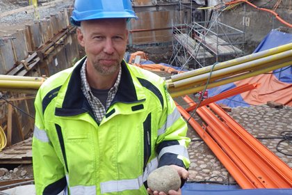 Arkelolog Johan Hedlund står i gropen vid södermalmstorg och håller en gatsten från 1600-talet i sin hand.