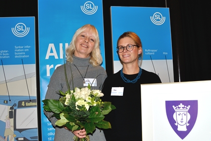 Två kvinnor med blommor i händerna framför SL-affischer.