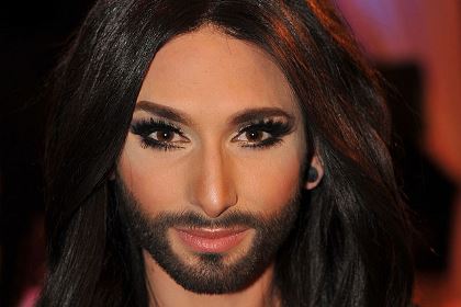 Conchita Wurst har långt, mörkt hår och helskägg. Hon pryder sitt ansikte med smink och lösögonfransar.