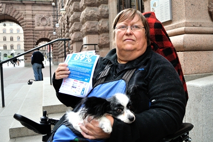 Madde Palmgren har kort blont hår och ovala glasögon. Hon sitter med en liten hund i famnen utanför Riksdagshuset med blå flygblad i handen där man ser texten 89 procent.